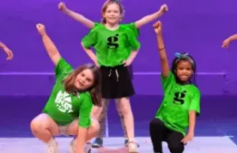 Group of kids performing on stage with purple lit background at A.D. Players Summer Theatre Camp.